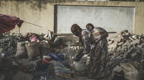 A gravel crusher carries her child on her back among slabs and smaller stones near the Cite ...
