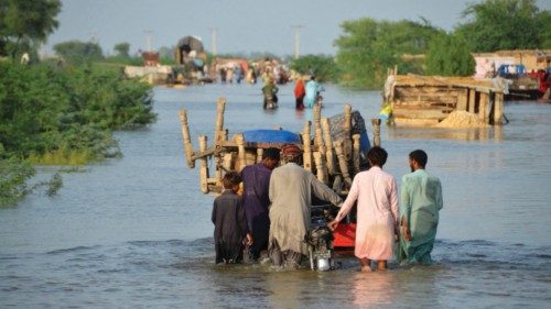 Men walk along a flooded road with their belongings, following rains and floods during the monsoon ...