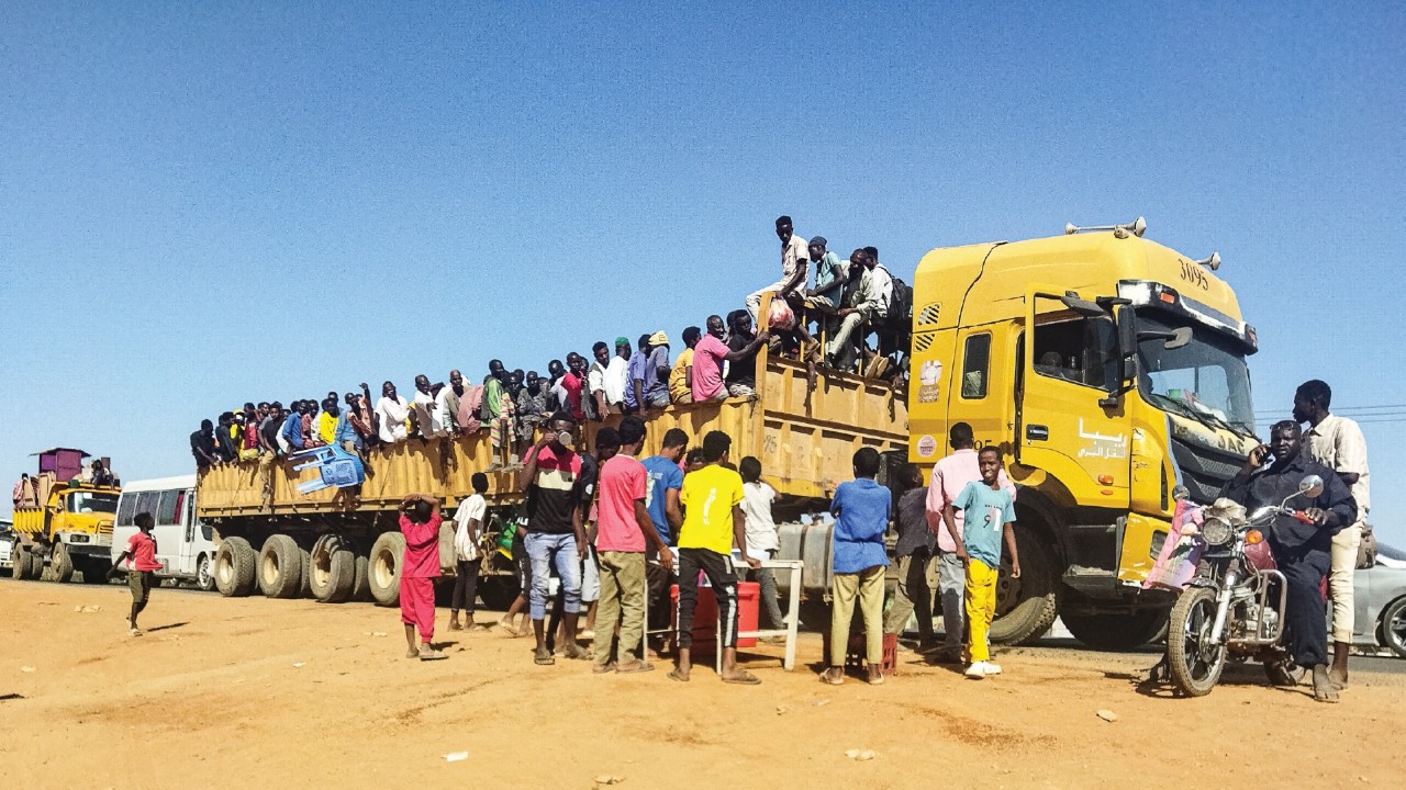 People displaced by the conflict in Sudan get on top of the back of a truck moving along a road in ...