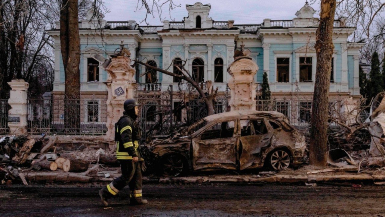 TOPSHOT - A Ukrainian rescuer walks by a burned car in front of damaged building at the site of a ...